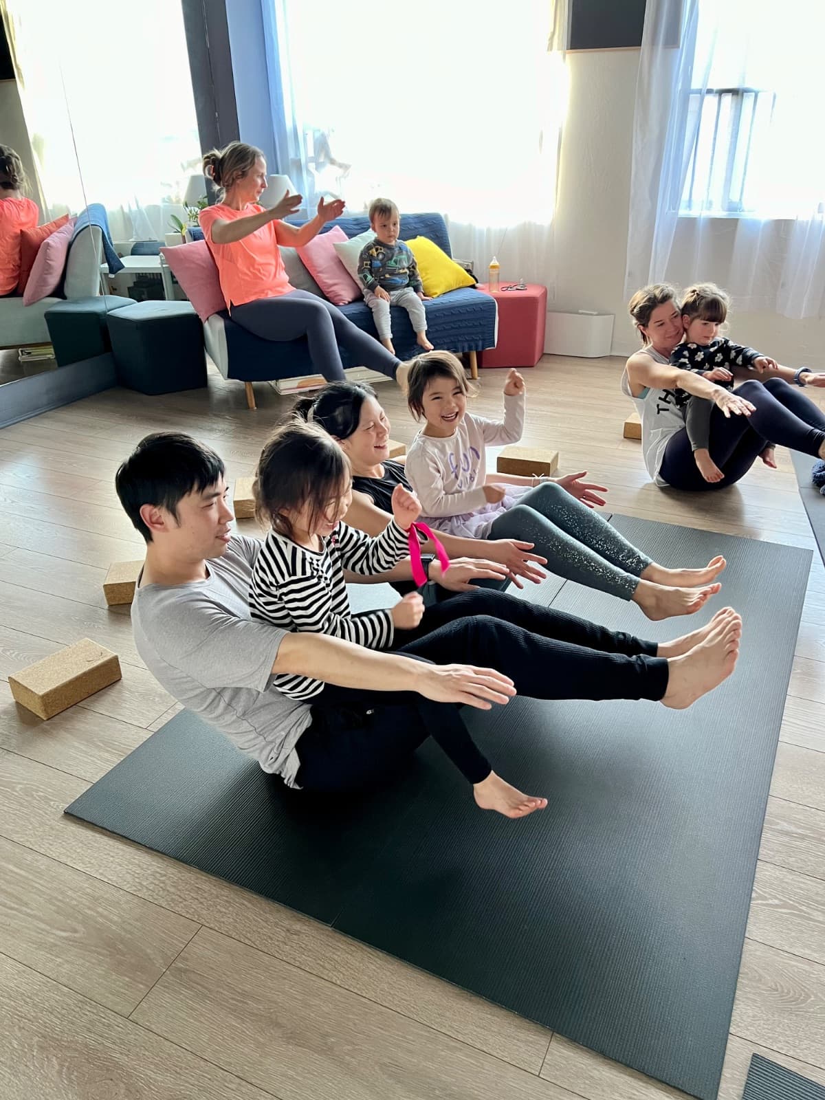 Families laughing while doing partner boat pose in family yoga class