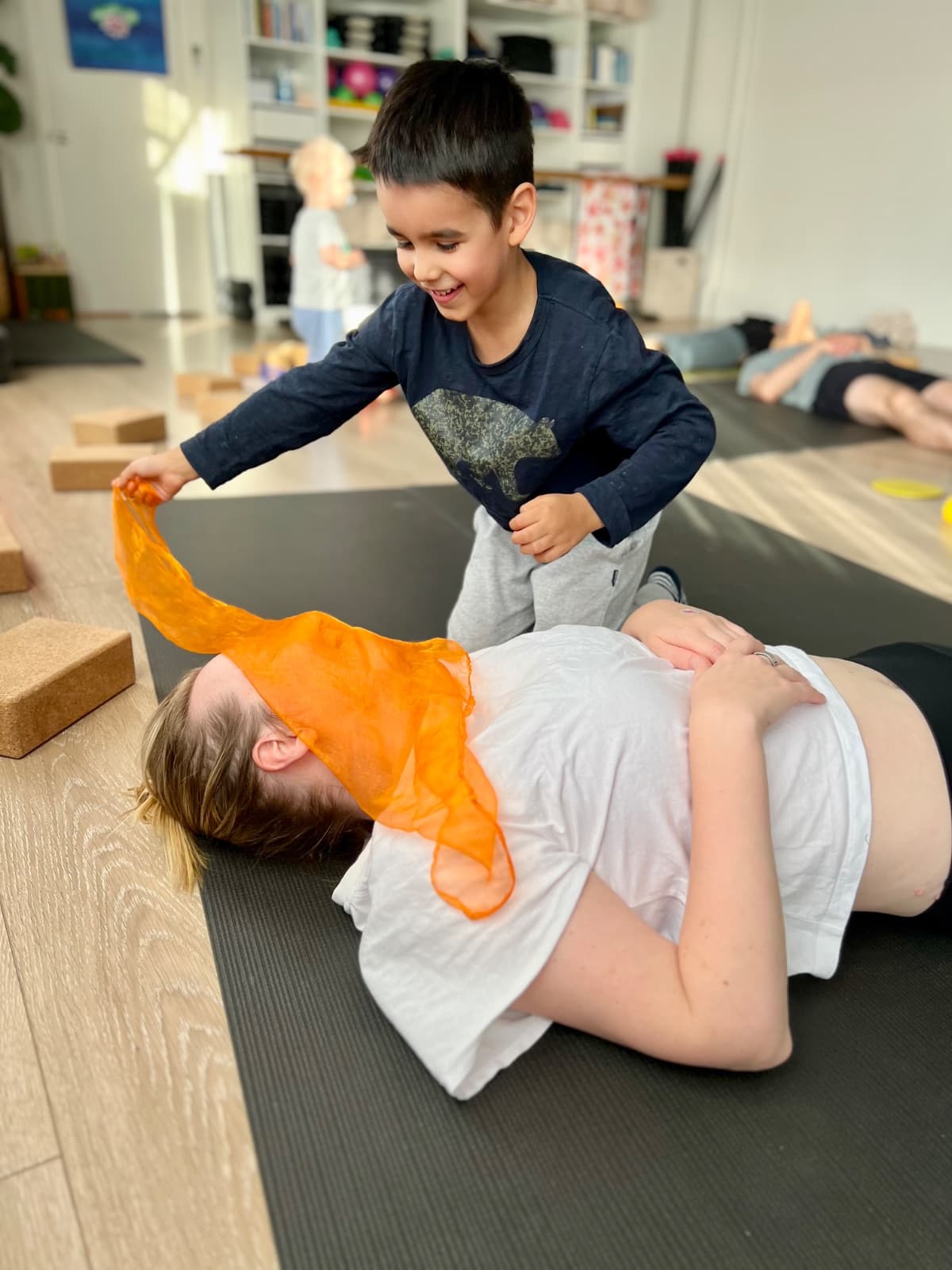 Child draping a scarf over parent during playful relaxation in family yoga
