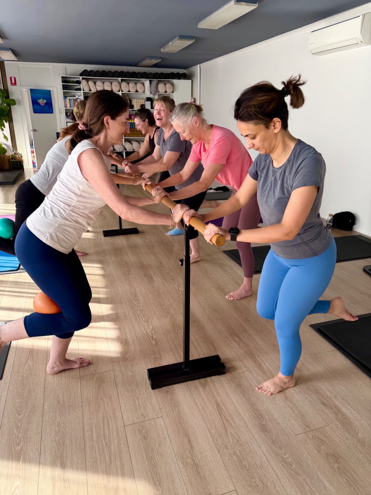 Barre class doing squats with Pilates ball at the barre in the Evolvere studio
