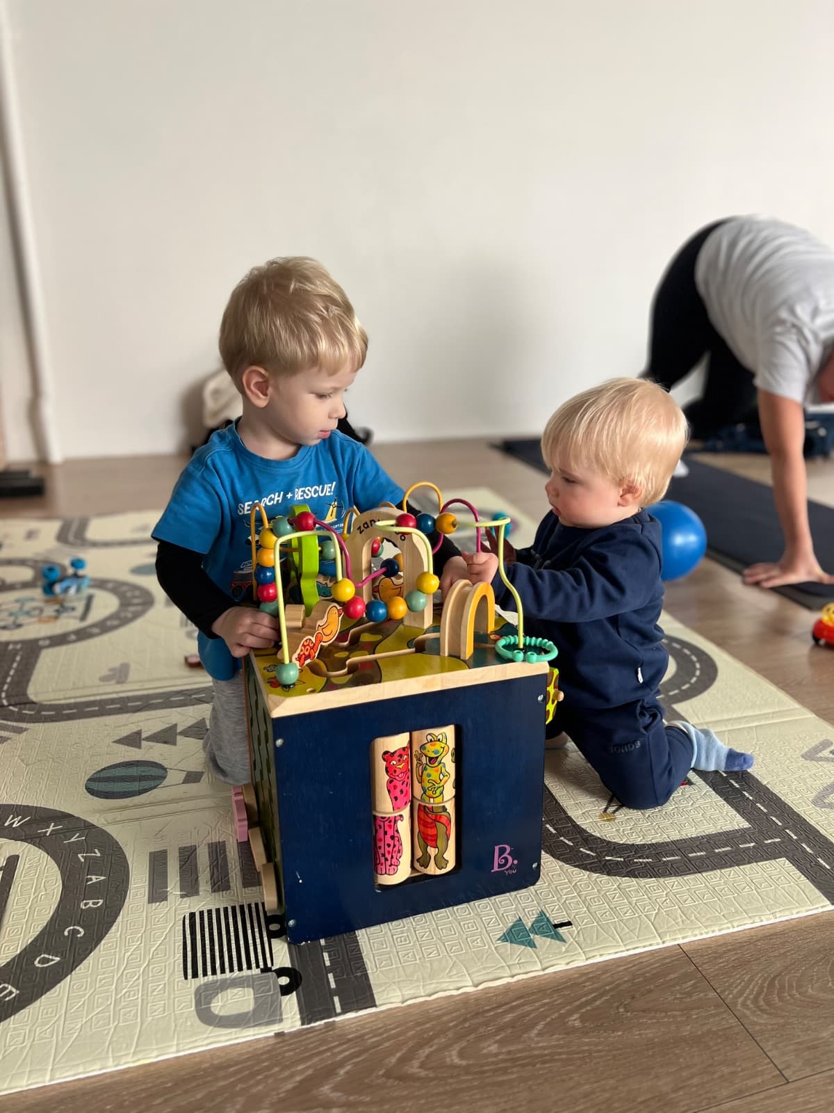 Toddlers playing with an activity cube while mum exercises in the background
